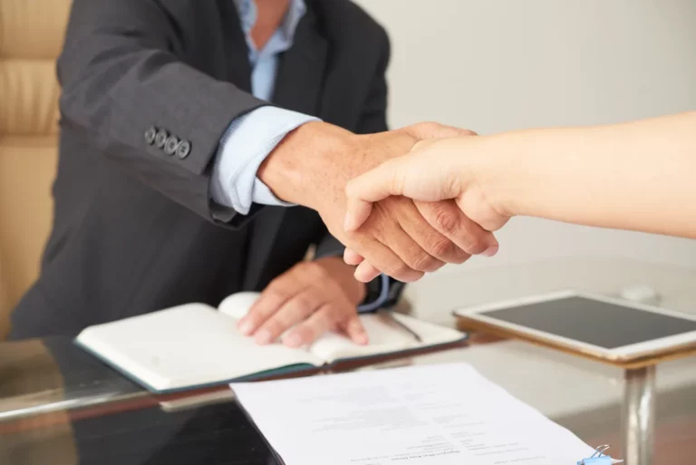 Two professionals shaking hands in a business office, symbolizing the trust-based relationship that drives dealership sales