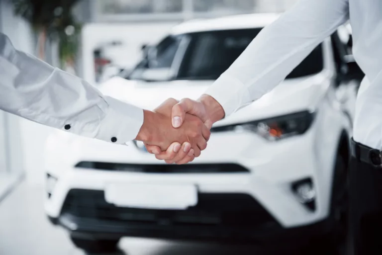 Professional car salesperson shaking hands with a buyer in a dealership showroom