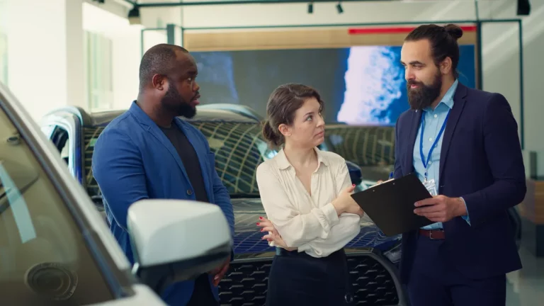 Sales consultant coaching two buyers on word tracks in a car dealership showroom