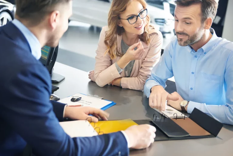 Couple meeting with a car dealer in a showroom discussing vehicle priorities and compromise