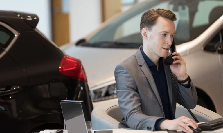 Car salesperson on the phone in a dealership showroom booking a future appointment