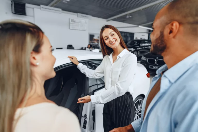 Car salesperson explaining vehicle features to buyers in dealership showroom